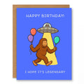 Bigfoot UFO Birthday Card Legendary showing Bigfoot holding balloons under a UFO beam of light with front cover text: Happy Birthday! I hope it’s legendary
